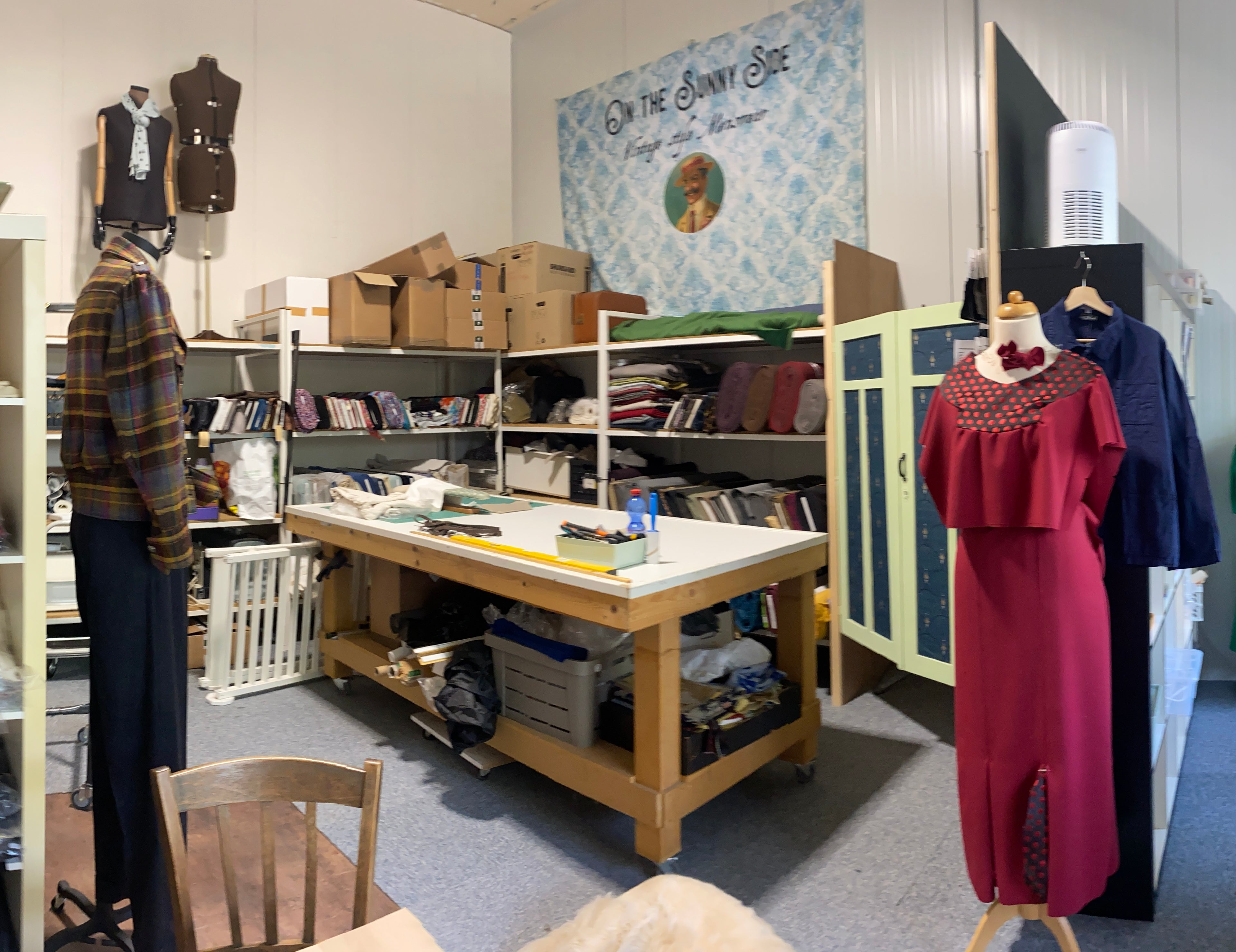 atelier with shelves, fabrics and clothing items including a red dress.