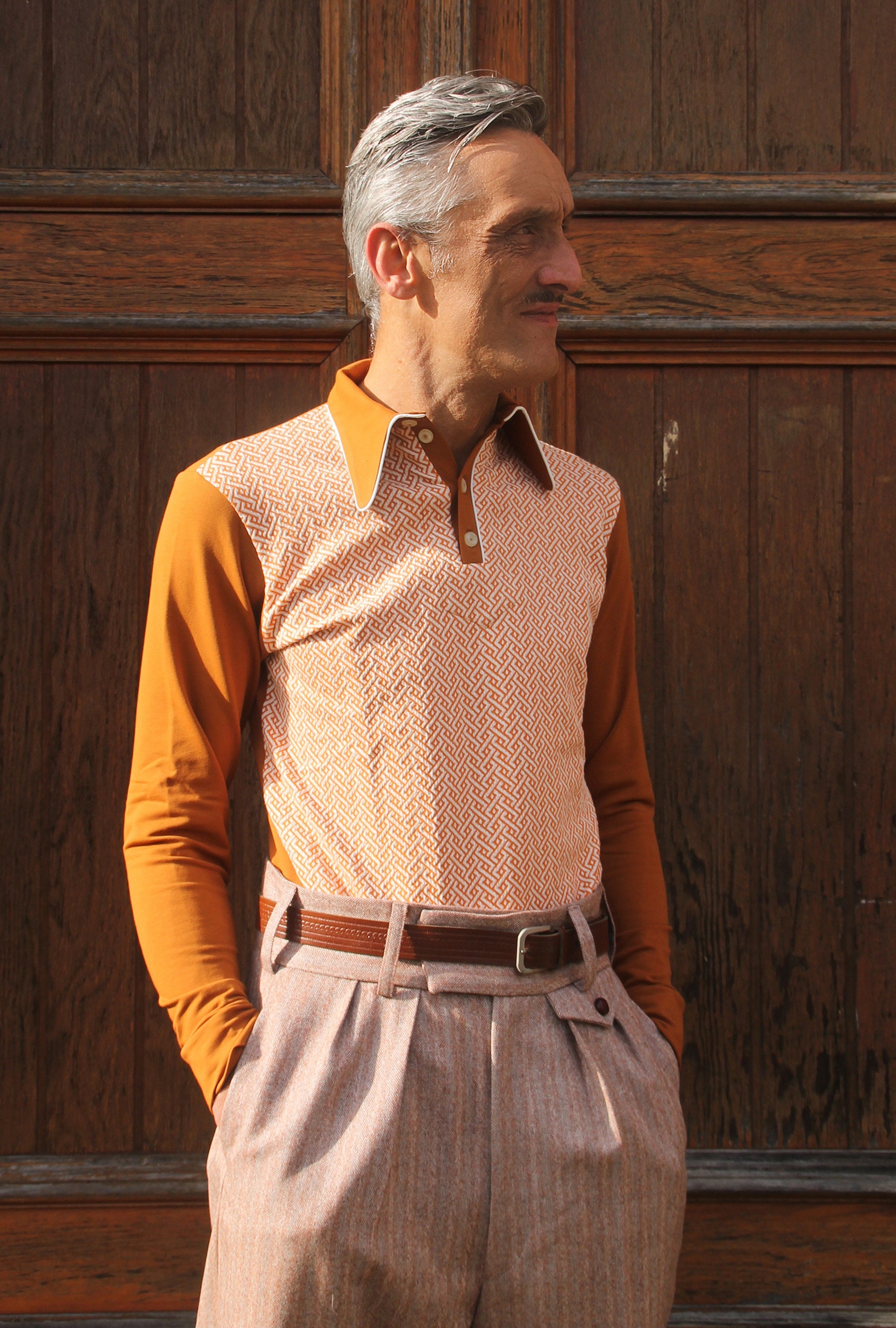 rust brown long sleeve polo shirt with pointed collar. The front panel is from 3D knit bio cotton with braid motif in orange and off white, the sleeves, collar and back are rust brown soft bio jersey with a french terry finish on the inside.