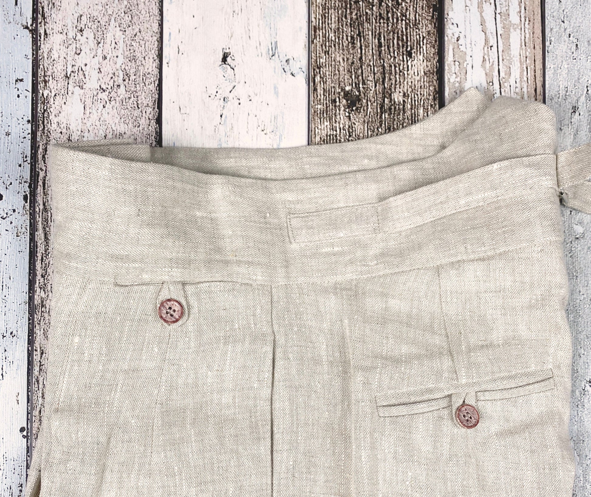 1930s style ladies suit pants for women in natural colored linen. These trousers are adapted from a 1930s mens pattern with wide fit, pleated front, very high waisted, fishtail back and buckle back. Close up from the side, showing front watch pocket with loop and button, the generous side pocket, the buckle on the back waistband and one back pocket.