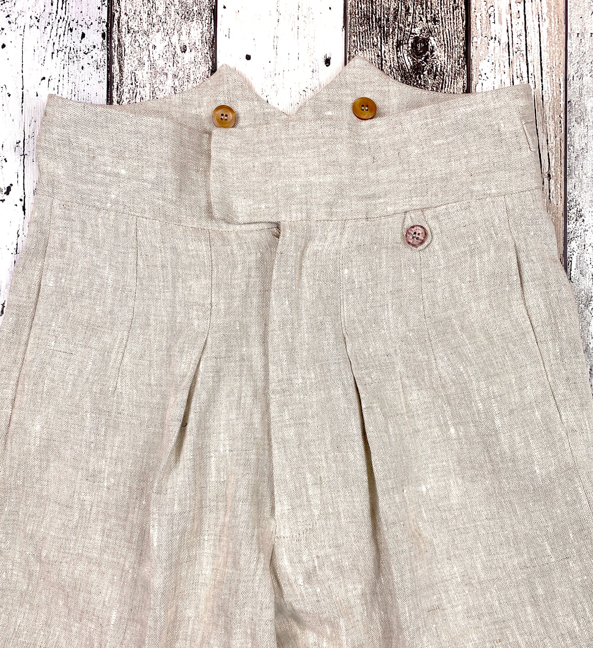1930s style ladies suit pants for women in natural colored linen. These trousers are adapted from a 1930s mens pattern with wide fit, pleated front, very high waisted, fishtail back and buckle back. Close up front, zipper closure like men&#39;s trousers, waistband overlapped closure with hook and eye, inward folded pleats