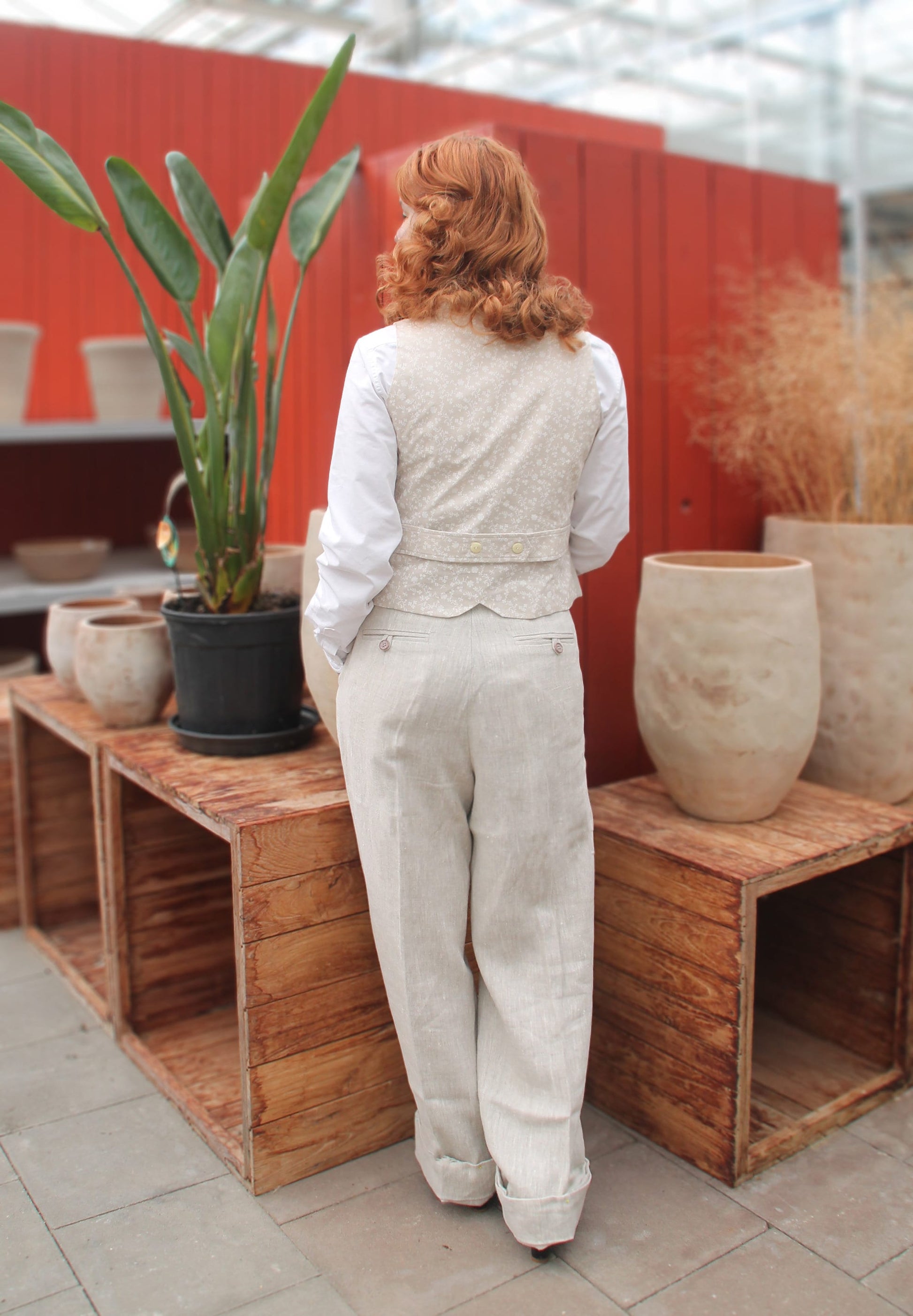1930s style ladies suit pants for women in natural colored linen. These trousers are adapted from a 1930s mens pattern with wide fit, pleated front, very high waisted, fishtail back and buckle back. The trousers are worn with a matching waistcoat. View from the back