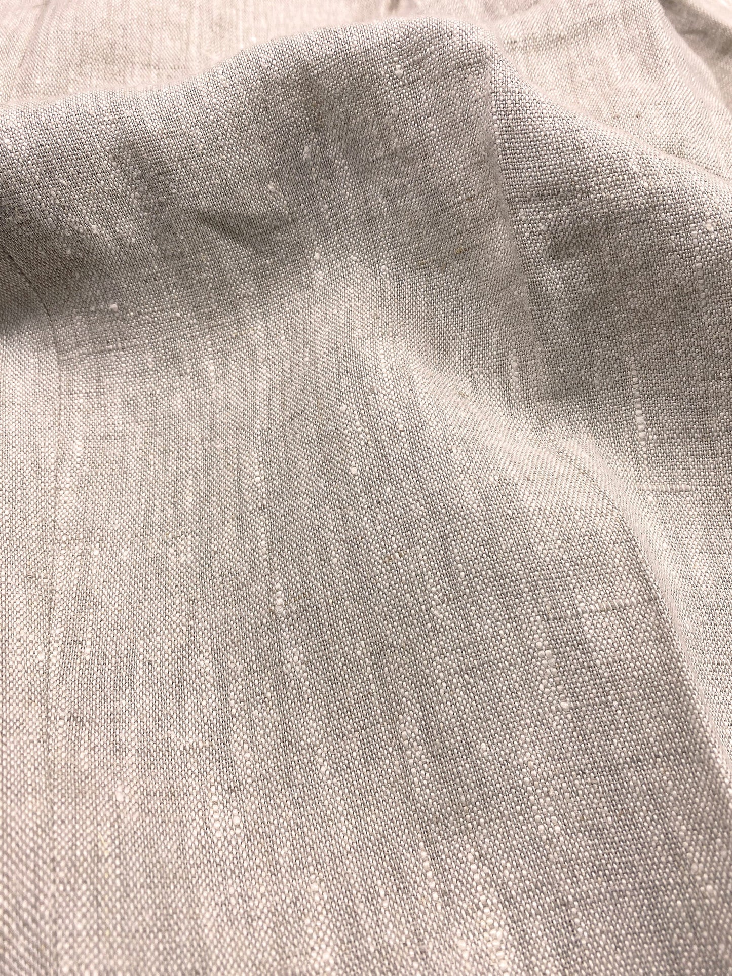 1930s style ladies suit pants for women in natural colored linen. These trousers are adapted from a 1930s mens pattern with wide fit, pleated front, very high waisted, fishtail back and buckle back. Close up of the fabric, showing a soft feeling linen fabric, with some irregular threats in a slightly lighter colour beige than the natural linen
