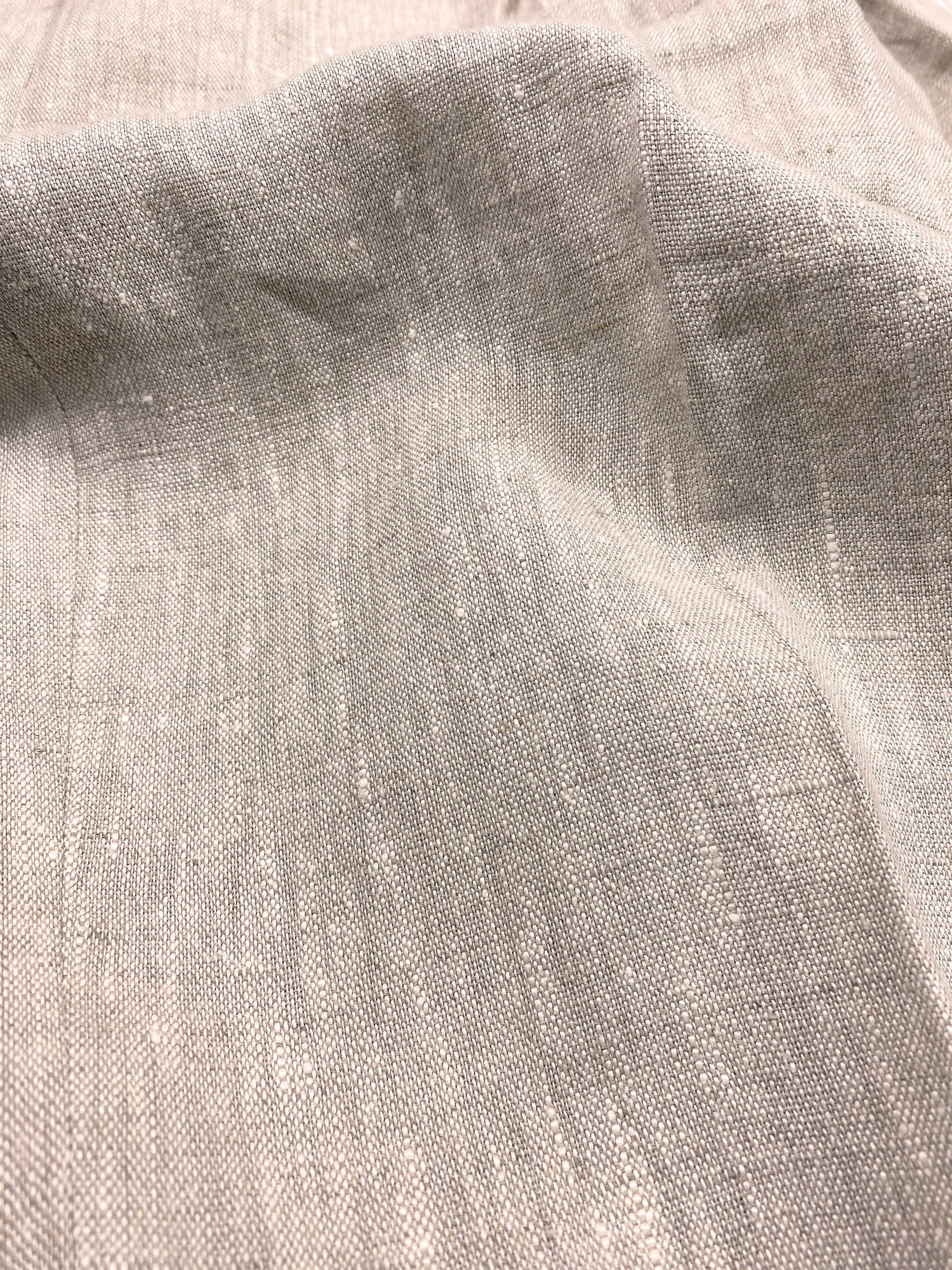 1930s style ladies suit pants for women in natural colored linen. These trousers are adapted from a 1930s mens pattern with wide fit, pleated front, very high waisted, fishtail back and buckle back. Close up of the fabric, showing a soft feeling linen fabric, with some irregular threats in a slightly lighter colour beige than the natural linen