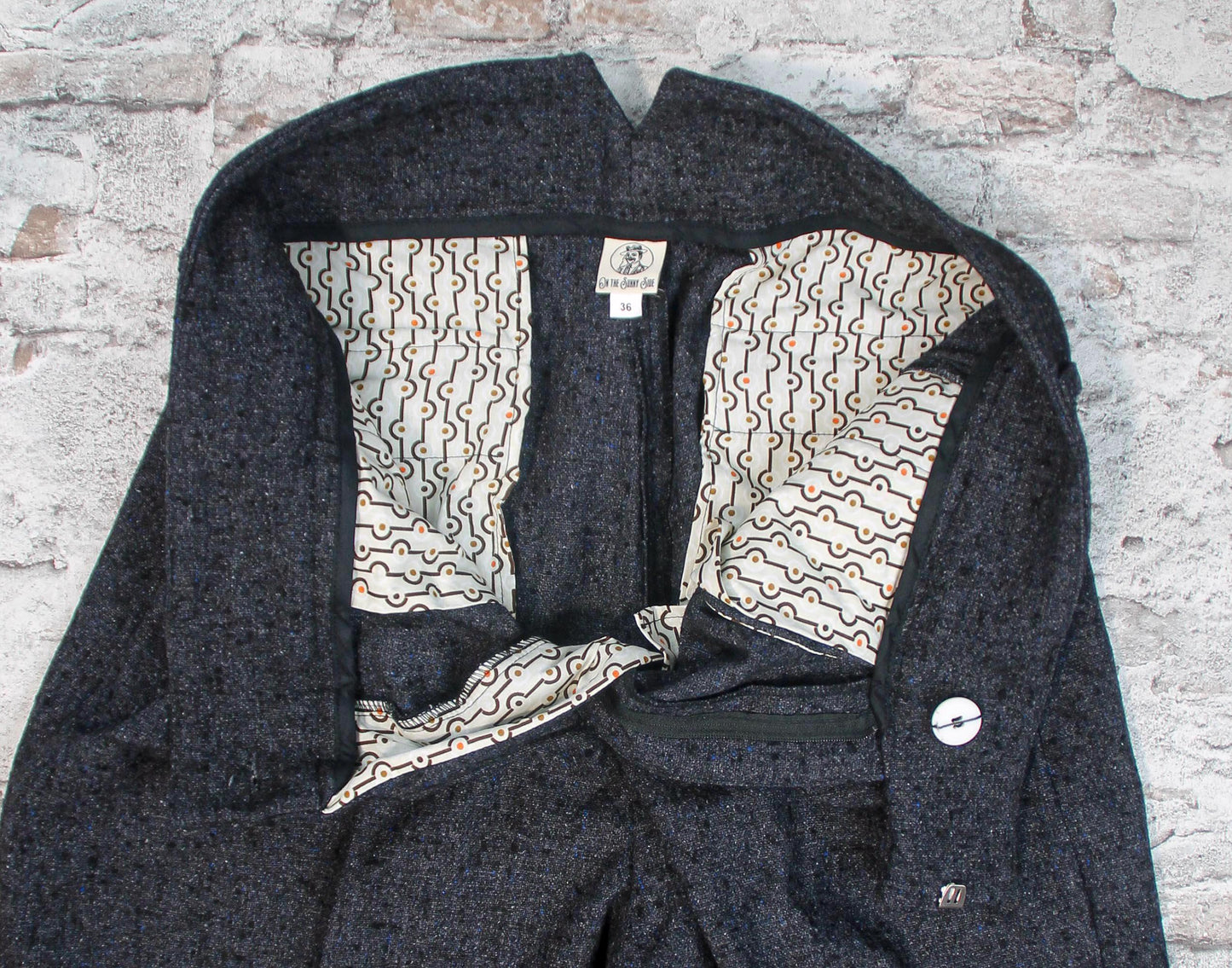 These high-waisted, pleated vintage-style trousers are made of rugged pure wool in a dark grey charcoal colour with small bright blue flecks.  The design is based on an original pattern from the 1940s with all the attention to details. Inside close up showing cotton pockets with art deco print