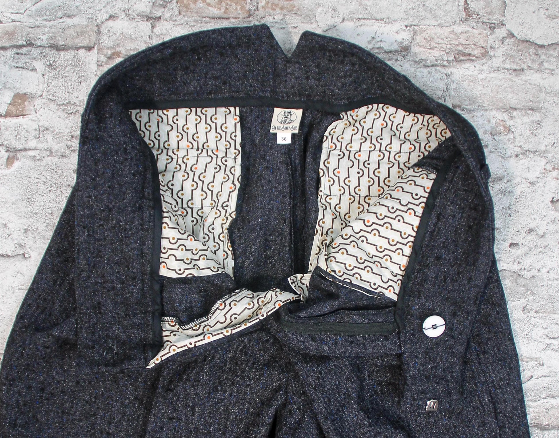 These high-waisted, pleated vintage-style trousers are made of rugged pure wool in a dark grey charcoal colour with small bright blue flecks.  The design is based on an original pattern from the 1940s with all the attention to details. Inside close up showing cotton pockets with art deco print