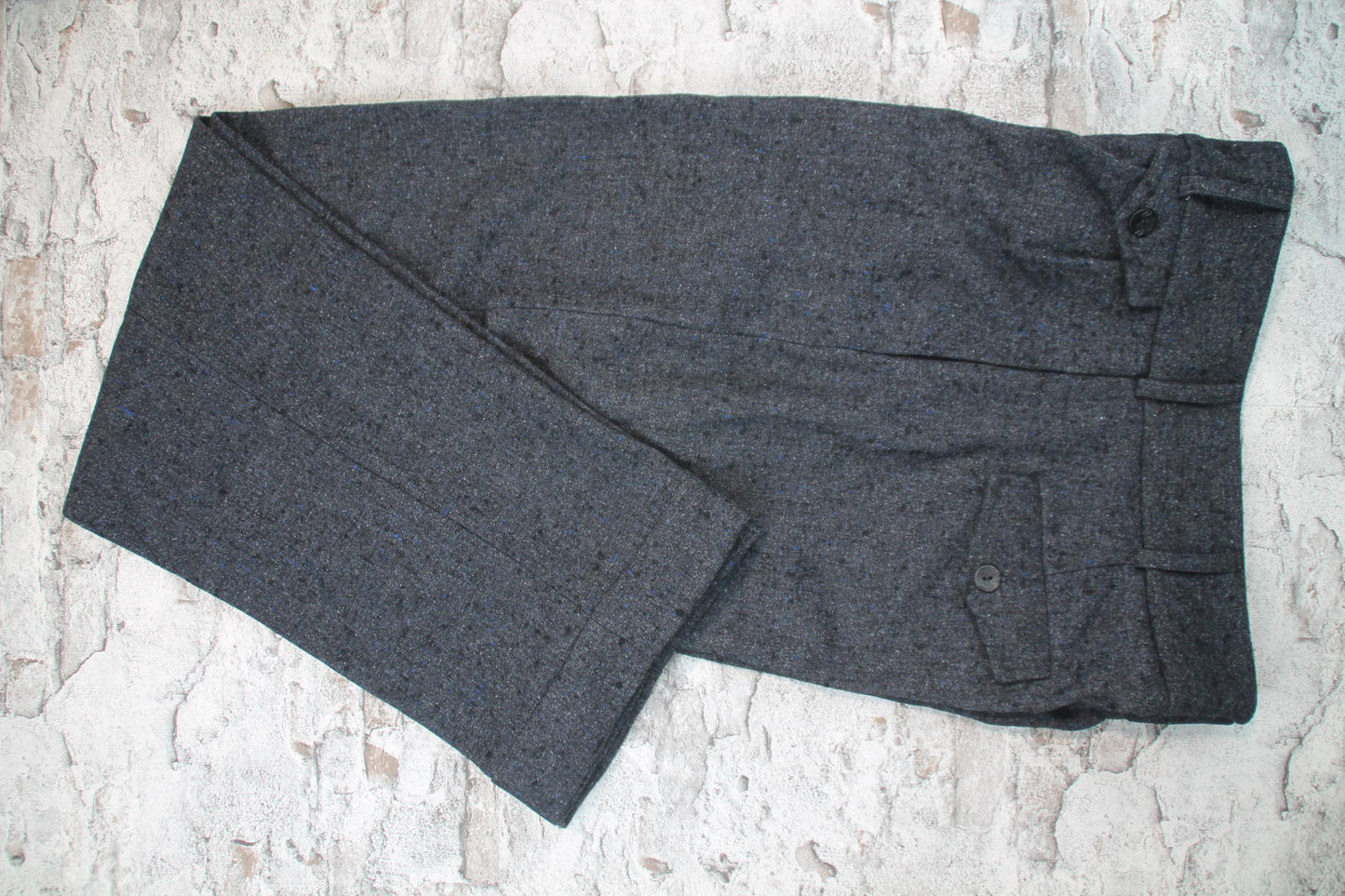 These high-waisted, pleated vintage-style trousers are made of rugged pure wool in a dark grey charcoal colour with small bright blue flecks.  The design is based on an original pattern from the 1940s with all the attention to details. They have 6 belt hoops for wearing with a belt. There are two generous side pockets, and a small change pocket at the front, as well as two back pockets. The buttons are made from coconut.