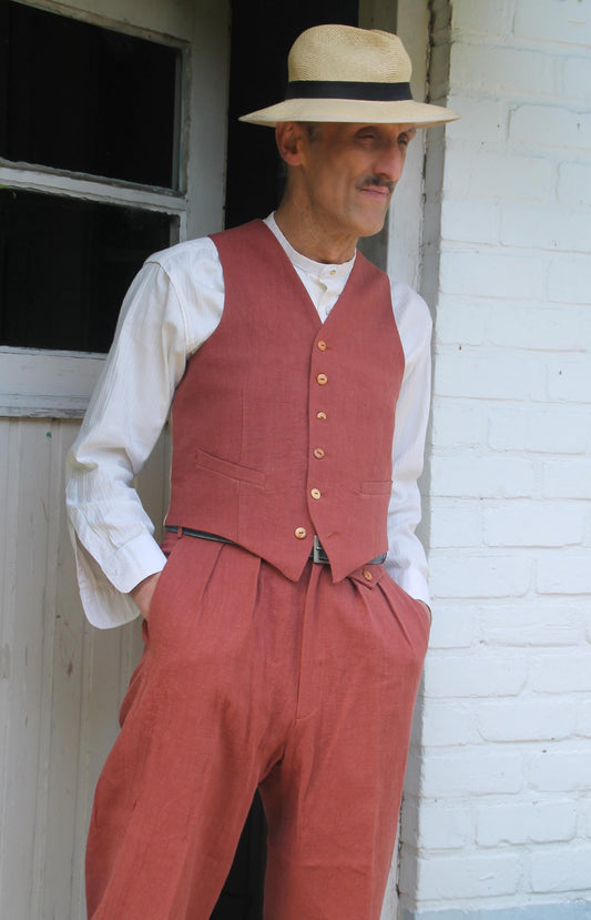 A man wearing a red linen waistcoat and matching trousers with a straw hat. The waistcoat has a button fastening and the trousers have pleats.